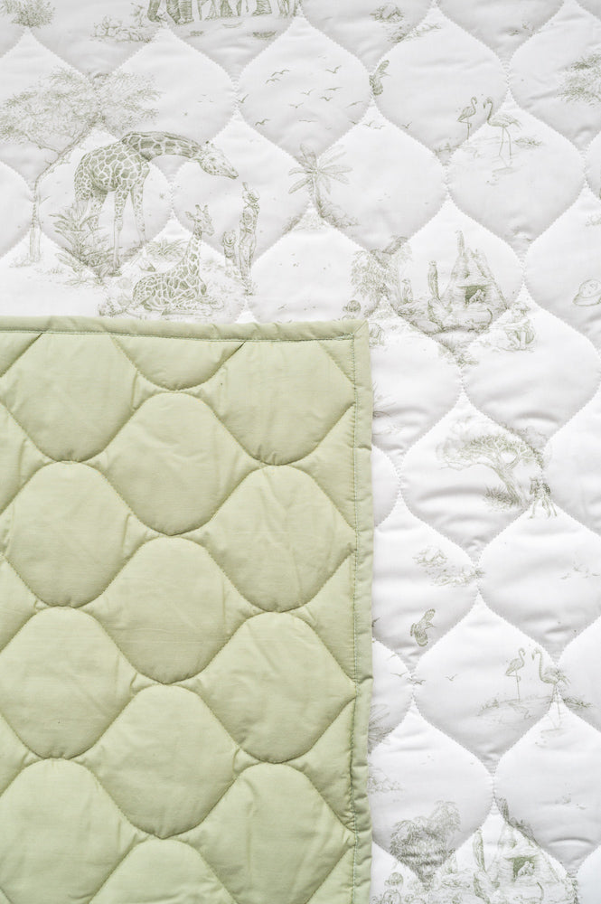 Close-up of the playmat’s pale green safari animal print and diamond quilting, with a corner showing the green reverse