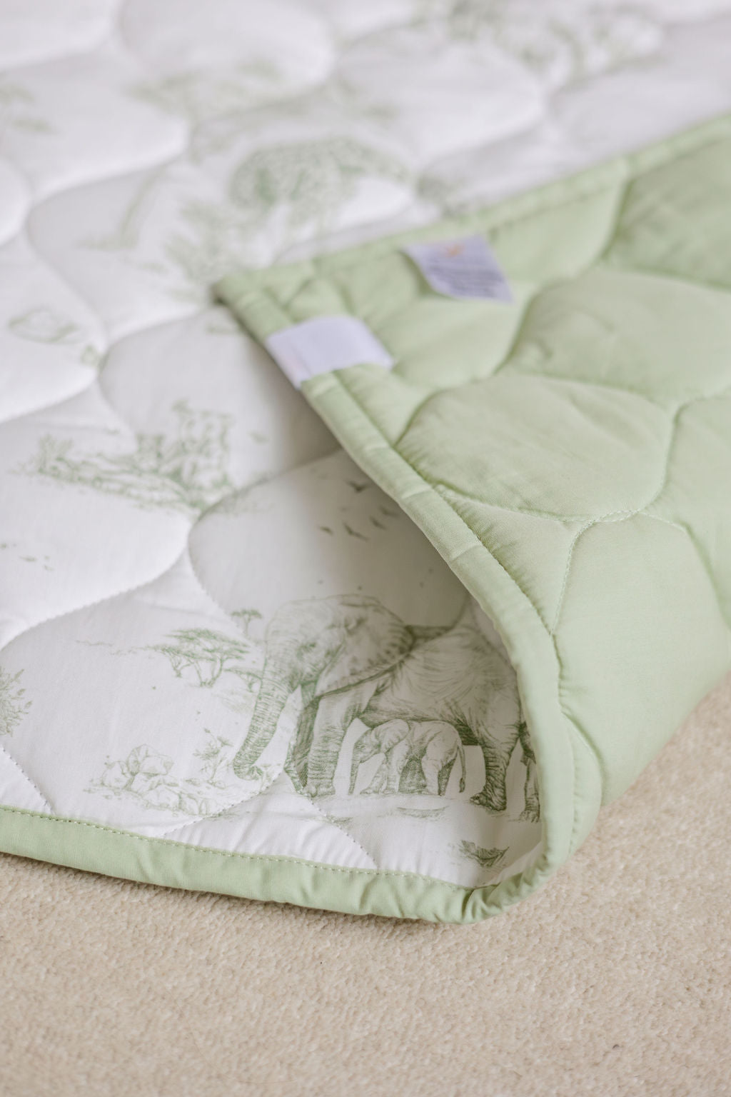 Safari Toile quilted playmat with a corner folded back to show its solid pale green reverse and matching edging.