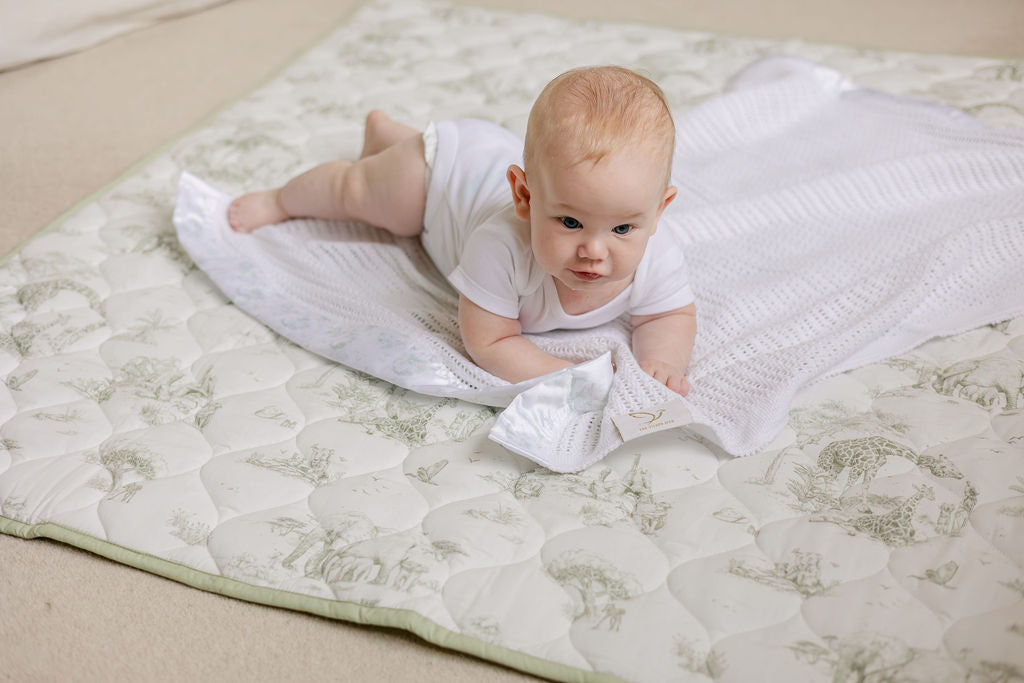 A quilted playmat with a safari theme, featuring an animal pattern, being used by an infant.