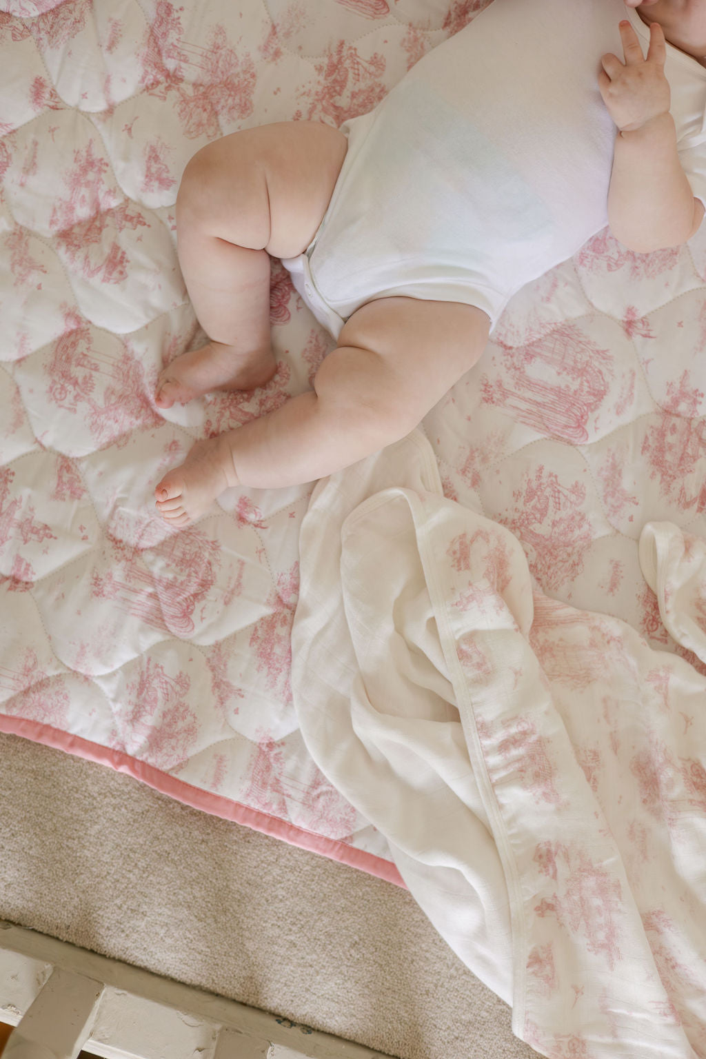 Close-up of a baby on the pink toile quilted playmat, showing its padded stitching and pink edging.