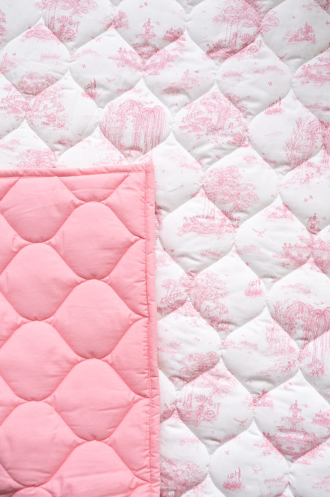 Close-up of the playmat’s pink pastoral toile print and diamond quilting, with a corner folded to show the pink reverse.