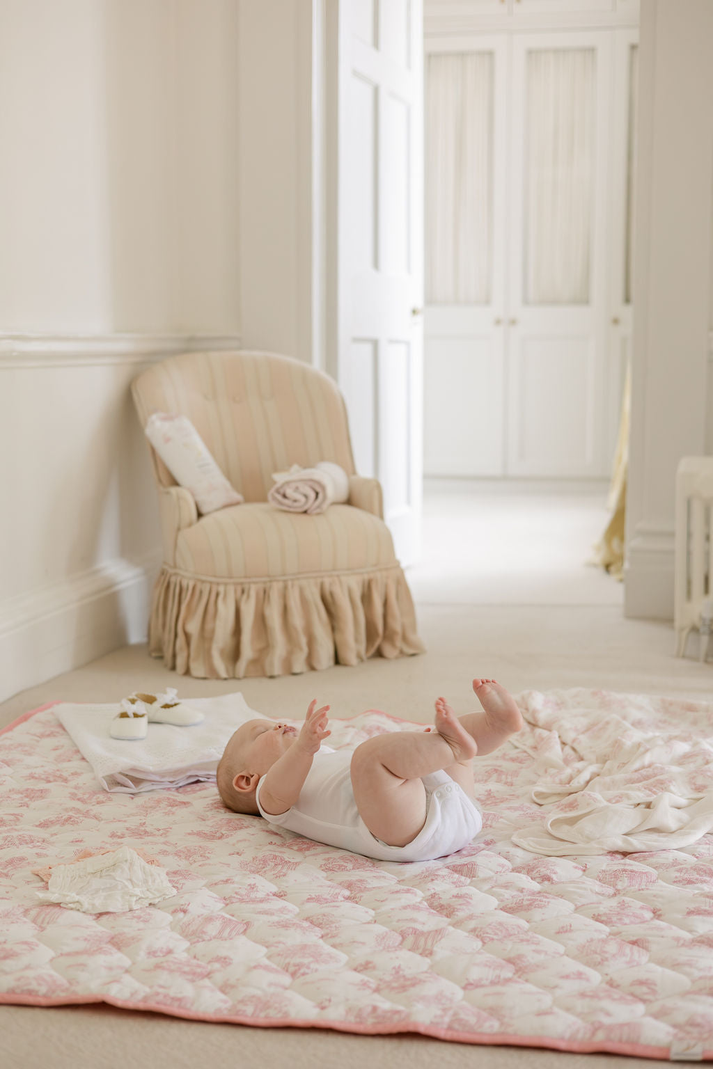 Baby lifting their legs while lying on the Spring Toile Pink quilted playmat in a cream nursery.